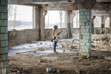 Fototapeta na wymiar a little girl alone in an abandoned and ruined building with a Kalashnikov assault rifle and arms making her way to survive