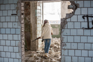a little girl alone in an abandoned and ruined building with a Kalashnikov assault rifle and arms...