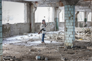 a little girl alone in an abandoned and ruined building with a Kalashnikov assault rifle and arms...