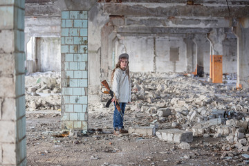 a little girl alone in an abandoned and ruined building with a Kalashnikov assault rifle and arms...