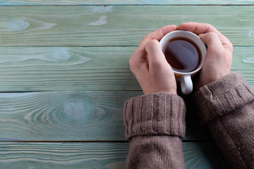 A young man warms his hands about a cup of hot tea