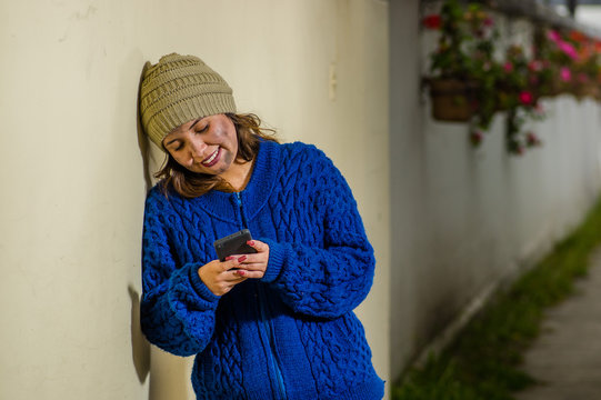 Outdoor view of homeless woman on the street in cold autumn weatherusing a celphone at sidewalk