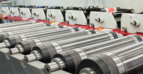Lined up magnetic cylinders for die cut on rotary printing press. Magnetic cylinder for flexo rotary die cutting. Magnetic roll and in-line press machine in background. Cylinder for cutting dies. - obrazy, fototapety, plakaty
