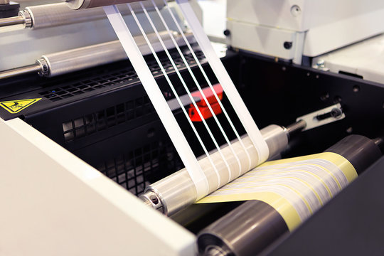 Close-up shot of labels manufacturing on flexo printing machine. Photo detail of matrix waste or trim removal from adhesive material on flexographic press.