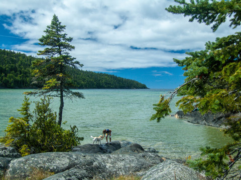 woman and dog on rocky shore, large river in background