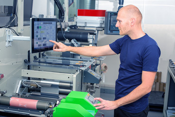 Worker next to the printing machine inputs the data by pressing the touch screen. Skilled printing...