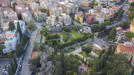 Aerial view of a small square with trees and meadows on either side of a road. The street passes under an ancient Rome arch.