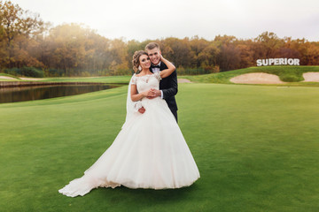 Fototapeta premium Husband embracing his beautiful elegant wife in wedding dress with lovely bouquet