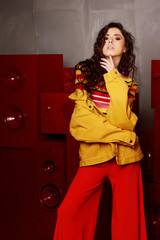 Studio fashion shooting.The girl in a bright outfit, top and pants flared in red and orange tones. Brunette with curly hair. Touching hands to the chin.