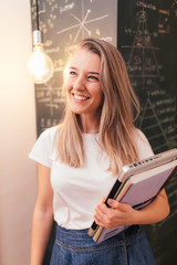 smiling student woman holding a laptop in front of a blackboard