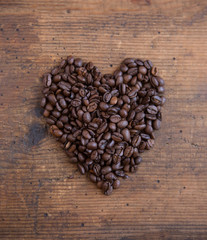 Coffee beans in the shape of a heart on wood table.  Overhead view. 