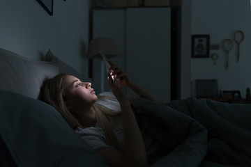 Sleepy exhausted woman lying in bed using smartphone at late night, can not sleep. Insomnia, nomophobia, sleep disorder concept. Addiction on social networks - obrazy, fototapety, plakaty