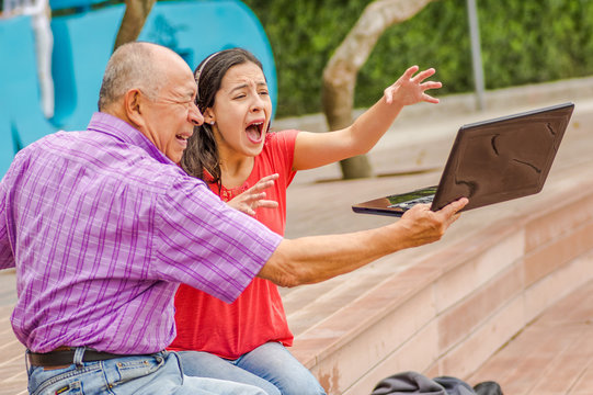 Outdoor view of father holding and computer and sacry daugher screaming afraid of his dad throw the computer in the ground, at park