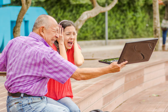 Outdoor view of father holding and computer and sacry daugher screaming afraid of his dad throw the computer in the ground, at park