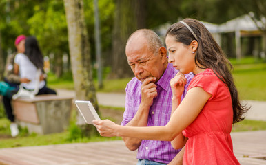 Outdoor view of father and daughter using a tablet looking somethings interesting, in the park