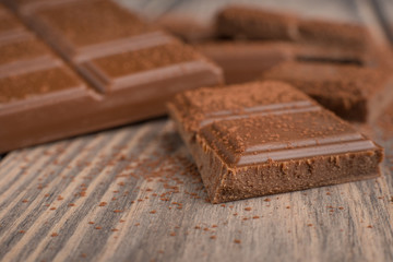 Milk chocolate with cocoa powder. On a wooden texture. Macro