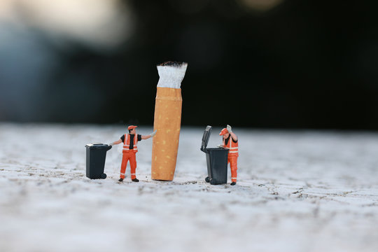 zwei Miniatur-M&uuml;llm&auml;nner m&uuml;ssen Zigarettenkippe entsorgen
