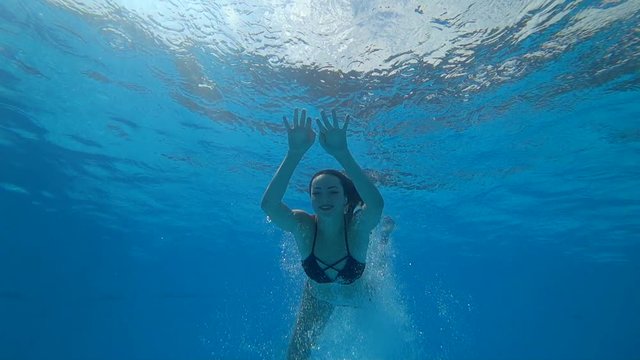 beautiful girl with open eyes float underwater at clear blue swimming-pool on background bubbles in summer