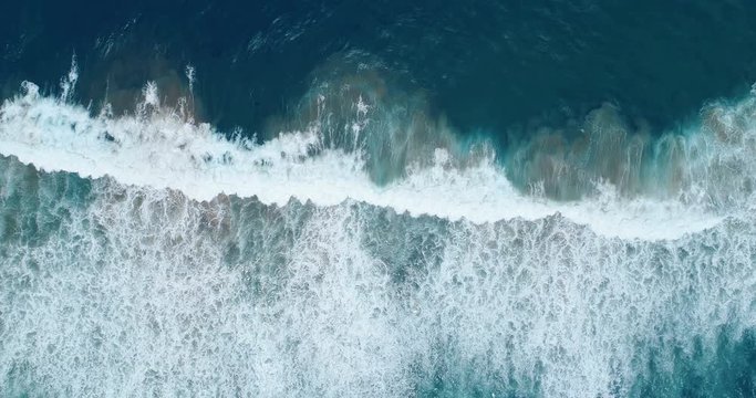 Vertical view of waves breaking just before the shore leaving trails of bubbles 4K aerial