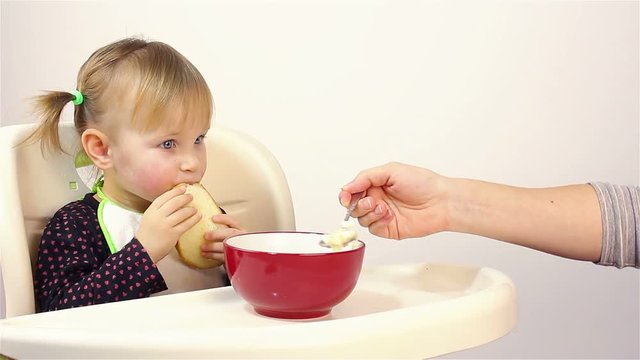 A small two-year-old girl eats porridge.
