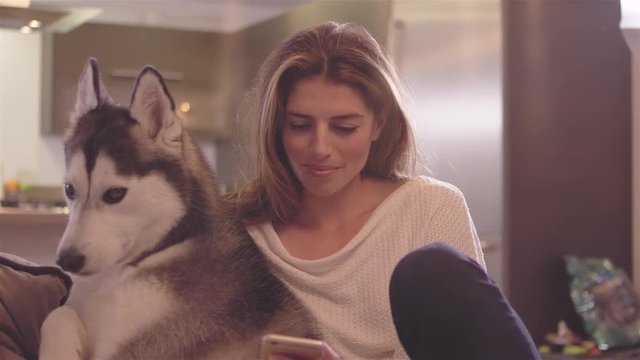 Beautiful young woman relaxing in her living room with her adorable dog, and using her cell phone