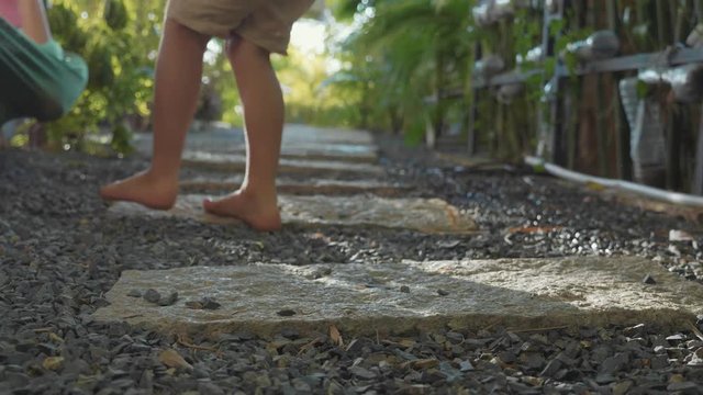Little girl walking on path in garden. Close-up feet go away from camera.