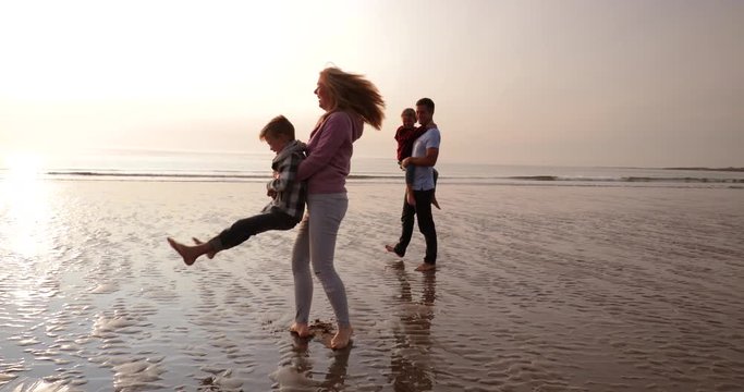 Slow motion of a family having fun and making memories at the beach while on holiday. Mother is spinning her son around, laughing and joking.