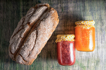 loaf of artisan bread and jars of jam on rustic wooden background