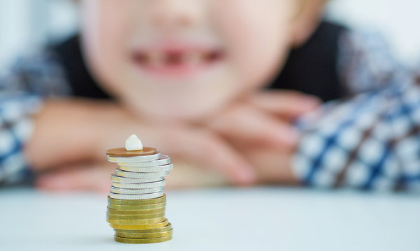 Smiling young boy with missing front tooth. Pile of coins with a baby tooth on top.