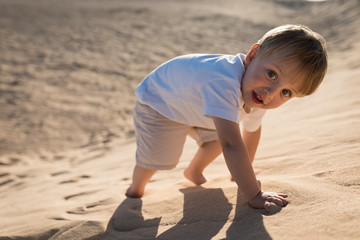 Handsome baby boy climbing on a sand dune.