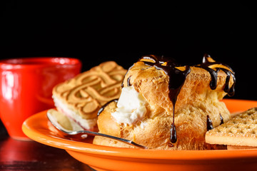 chocolate eclair and orange shortbread cookies on a plate next to a cup of coffee on a wooden...