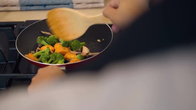 Balinese woman cooking fried broccoli, carrot and mushrooms on moden gas stove