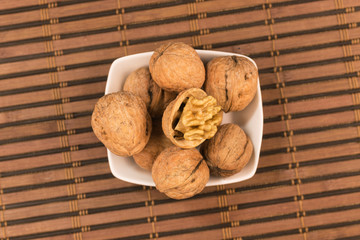 Pile of walnuts in a plate standing on a bamboo mat.