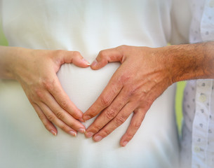 Heart shaped hands over a belly of pregnancy - hands of a man and a woman joined together in a heart shape over the belly of a pregnant woman