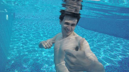 Happy man showing thumbs up under water, swimming in pool, summer recreation