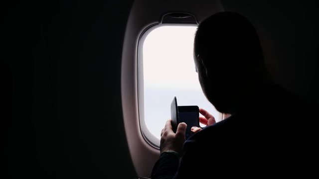 Silhouette of a man taking pictures from the window of an airplane, looking out of the window