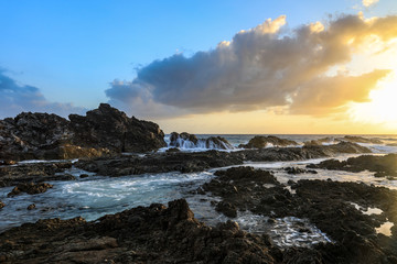 Ocean and rocky coastline against cloudy sky at sunrise