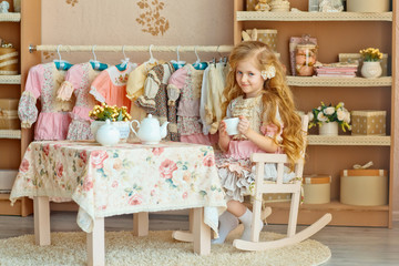 A little girl with light long hair drinking tea at the table. Stylized as a room of the last century. The Style Of Provence.