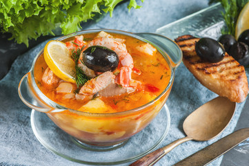 French fish soup Bouillabaisse with seafood, salmon fillet, shrimp with a rich flavor, with croutons. Delicious dinner in a transparent glass plate.