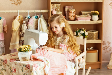 a small blonde girl with long hair smiling beautiful girl 6 years in a retro dress sew on a sewing...