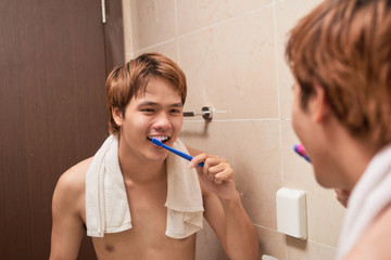 Brushing teeth in the morning.  Attractive young man brushing teeth with toothbrush, looking at himself in mirror