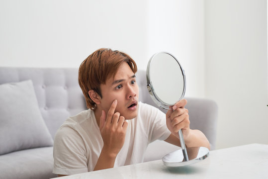 Handsome man looking at himself in mirror. Squeezing pimple.