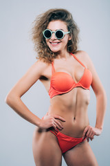 Fototapeta premium Young woman in sunglasses with beautiful slim perfect body in bikini isolated gray background