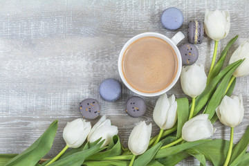 Cup of coffee, white tulips and gray macaroons on light wooden surface