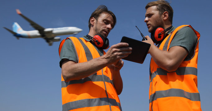 Airport Team Activity, Men Work on Digital Tablet, Talk on Walkie Talkie Collaborating with Air Traffic Control Tower, Airplane Flying Over Aircrew Controllers Ground Crew, Aircraft Passing Overhead