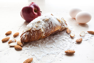 Fresh croissant on the table with sugar powder on it , eggs, almonds and apple on the table beside
