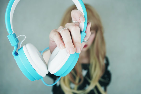 Chica joven y rubia sujetando unos auriculares con sus manos