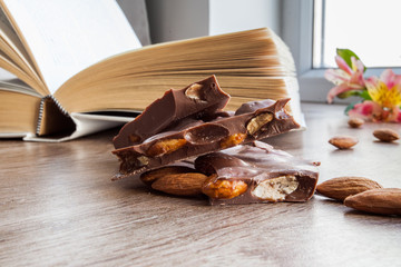 Chocolate with almonds close up, together with a book and flower on a background by the window