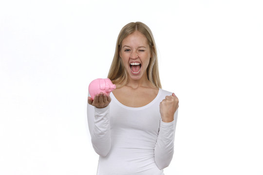 H&uuml;bsche blone Frau h&auml;lt ein Sparschwein in den H&auml;nden ballt eine Faust und ist begeistert