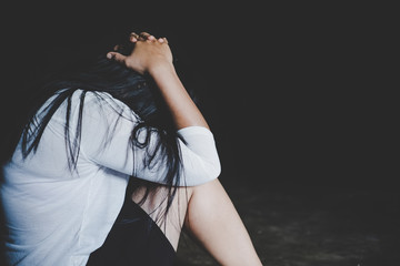 Young barefoot woman sitting at the floor embracing her knees, near full length window at home, her head down, bored, troubled with domestic violence, unwilling pregnancy, abortion, trolling